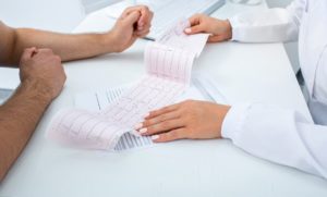 A photo of two people with their hands on a desk looking at a test result for heart rate or heart rhythm. 