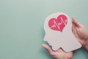 Conceptual Image of Hands Holding a Paper Head with a Red Paper Heart in the Brain Area with EKG Lines Going Across the Heart