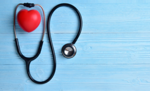 Heart-Shaped Stress Ball Inside the Ear Pieces of a Stethoscope Lying on a Light Blue Wooden Surface