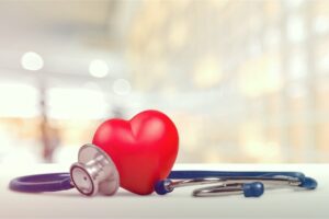 A Stethoscope Wrapped Around a Plastic Red Heart on Top of a White Surface with a Blurred Background