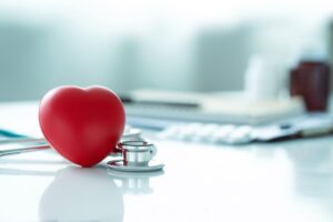 Conceptual Image of a Stress Ball Shaped Like a Heart on a Desk Next to a Stethoscope with Blurry Objects in the Background