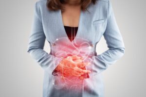 Torso of a Woman in a Blazer Holding Her Hands Over Her Stomach with an Illustration of a Stomach and Intestines Over It