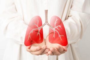 The Torso of Someone in a White Surgical Gown with their Hands Out Facing Up and an Illustration of Lungs Floating Over Them 