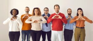 Seven people standing in a row with their hands in the shape of a heart in front of their chests.