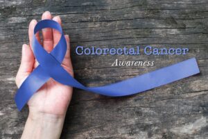 A hand holding a blue ribbon next to the words Colorectal Cancer Awareness 